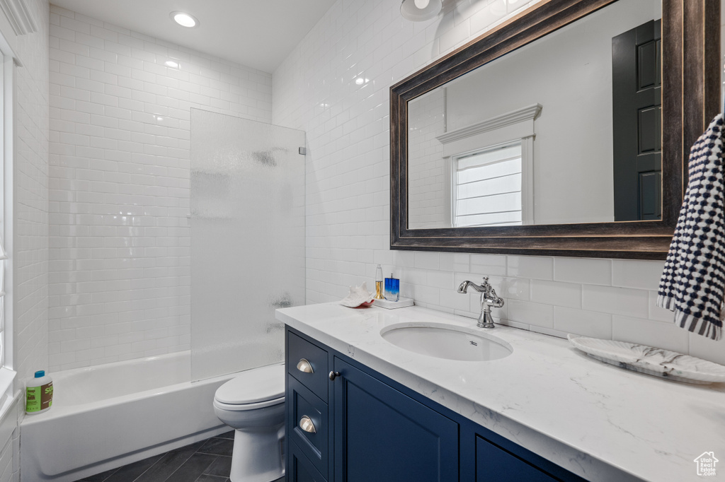 Full bathroom with tile flooring, tile walls, tiled shower / bath combo, toilet, and vanity