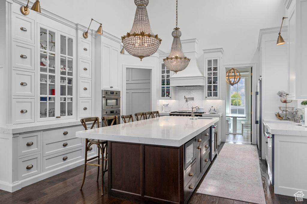 Kitchen with white cabinets, backsplash, a breakfast bar area, decorative light fixtures, and dark hardwood / wood-style flooring