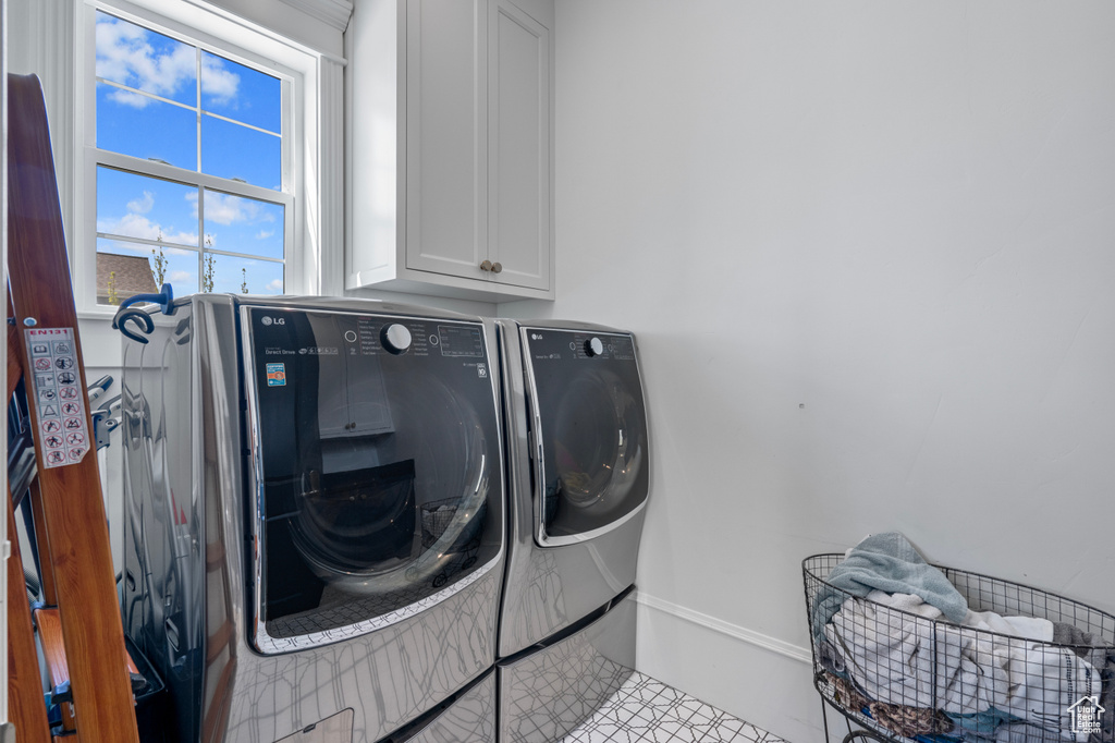 Laundry room with washing machine and clothes dryer, cabinets, and light tile floors