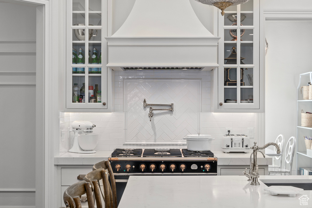 Kitchen featuring gas stove, custom range hood, tasteful backsplash, light stone counters, and sink