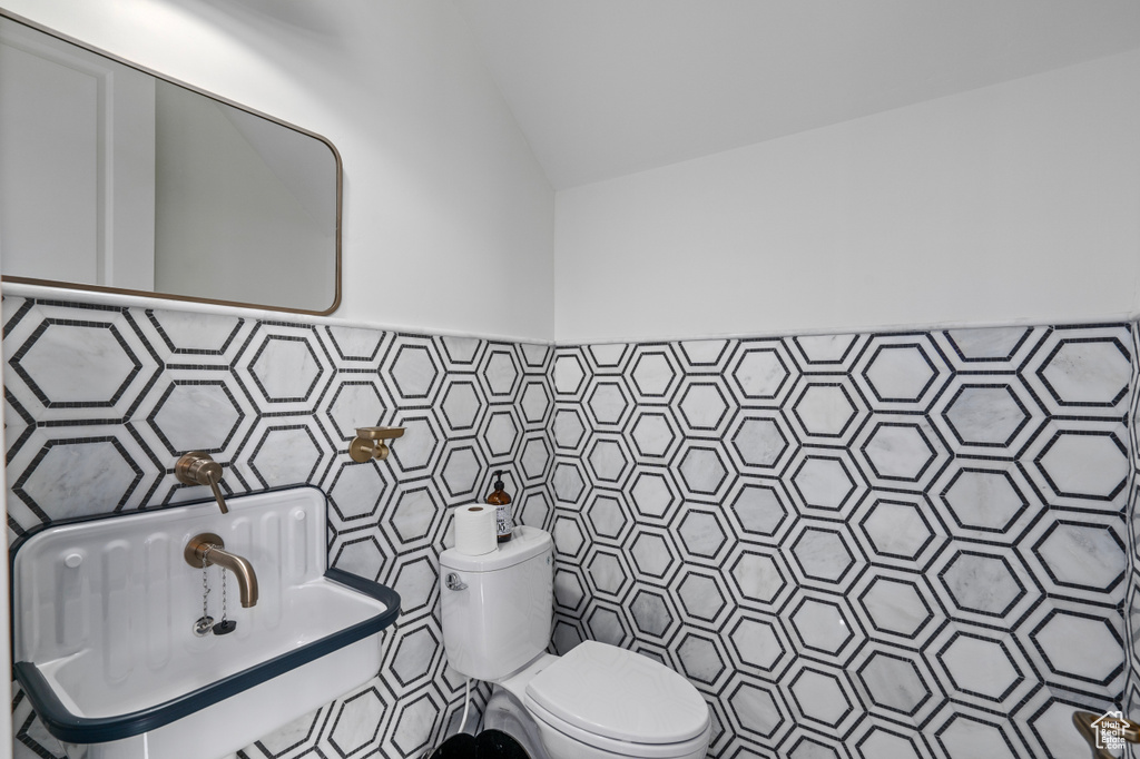 Bathroom with vaulted ceiling, tile walls, backsplash, and toilet