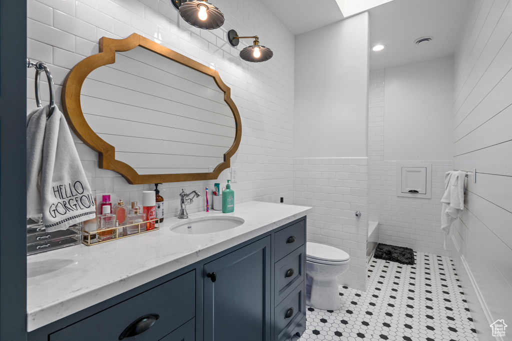 Bathroom featuring toilet, tile flooring, tile walls, and dual vanity