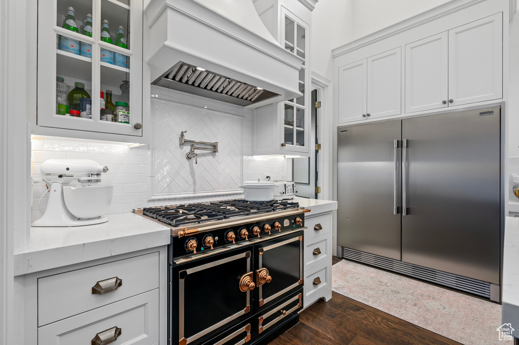 Kitchen featuring premium range hood, white cabinets, dark wood-type flooring, high quality appliances, and tasteful backsplash