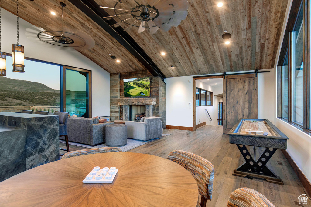 Dining room featuring wood-type flooring, a stone fireplace, a barn door, wood ceiling, and ceiling fan