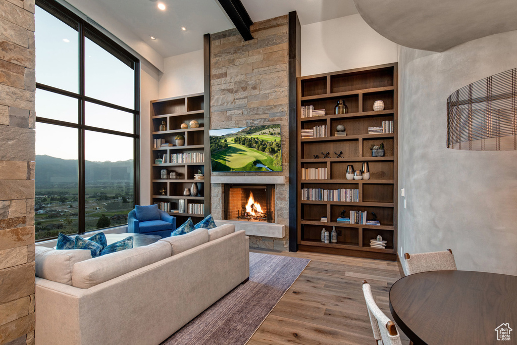 Living room with light hardwood / wood-style floors, built in features, beam ceiling, a stone fireplace, and a towering ceiling