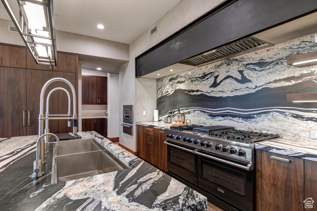 Kitchen with custom range hood, tasteful backsplash, stainless steel microwave, double oven range, and sink