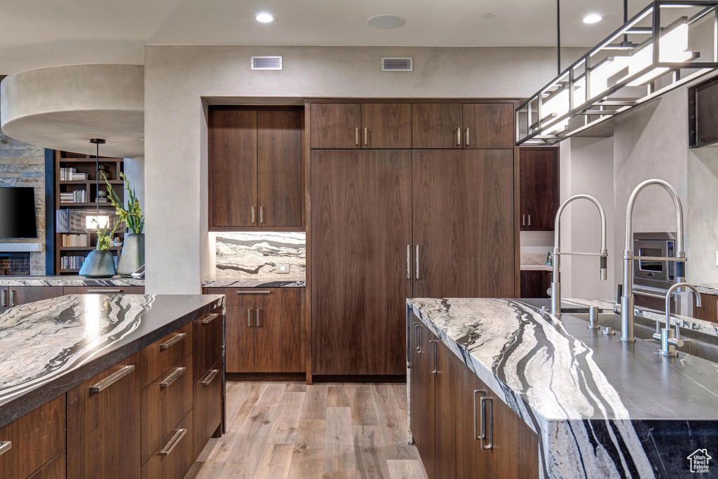 Kitchen featuring sink, dark stone counters, light wood-type flooring, and pendant lighting