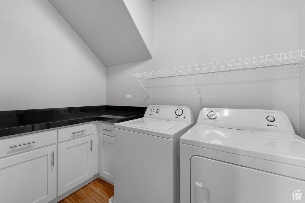 Laundry room with washing machine and dryer, cabinets, and light wood-type flooring