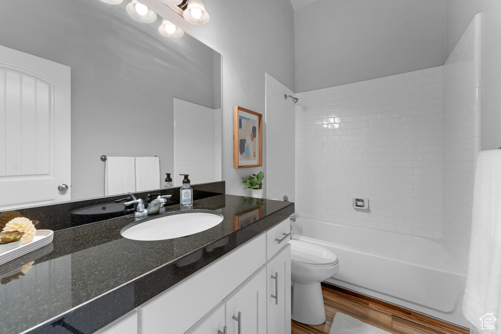 Full bathroom with wood-type flooring, tiled shower / bath, vanity, and toilet