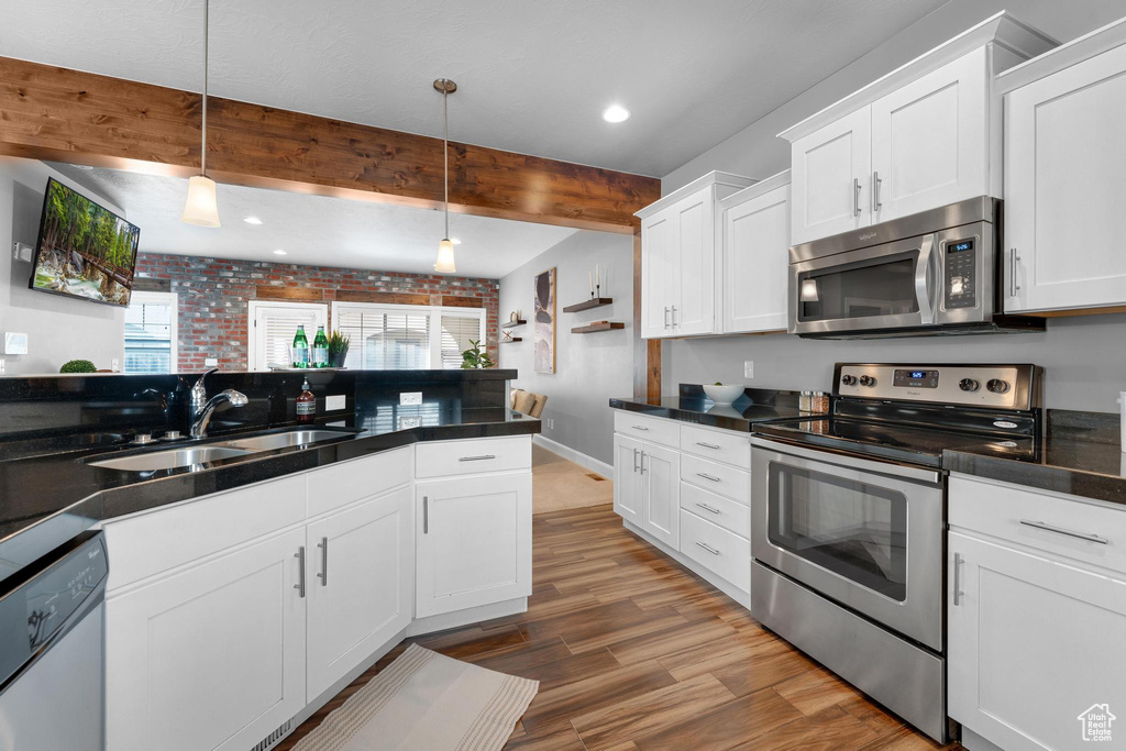 Kitchen with white cabinetry, brick wall, stainless steel appliances, beam ceiling, and sink