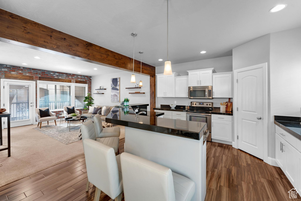 Kitchen featuring decorative light fixtures, stainless steel appliances, brick wall, white cabinets, and dark carpet