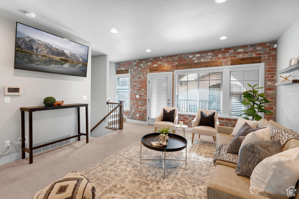 Carpeted living room featuring brick wall