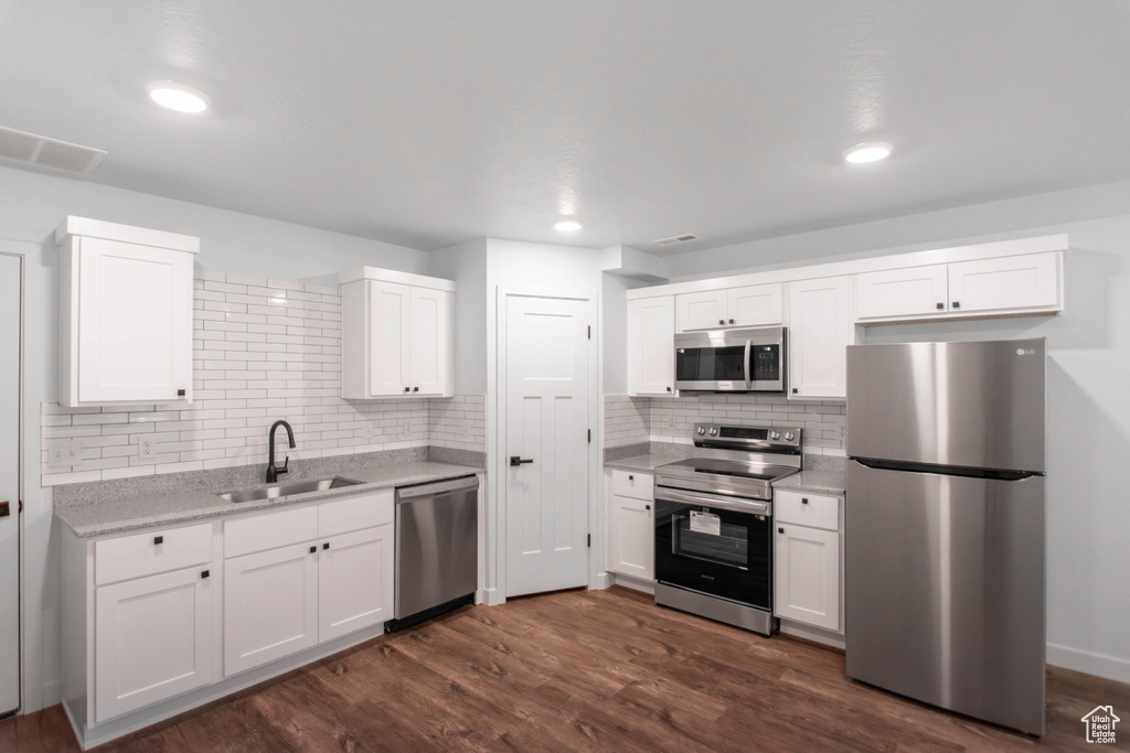 Kitchen with appliances with stainless steel finishes, dark hardwood / wood-style flooring, sink, and white cabinets