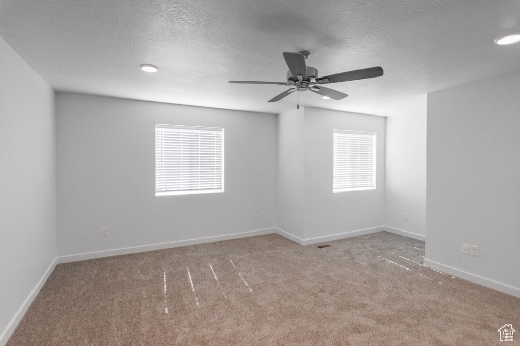 Empty room with ceiling fan, light colored carpet, a textured ceiling, and a healthy amount of sunlight