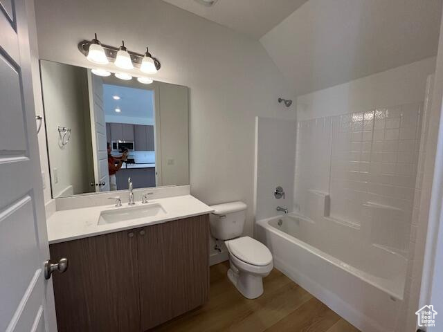 Full bathroom featuring hardwood / wood-style floors, bathtub / shower combination, lofted ceiling, toilet, and vanity