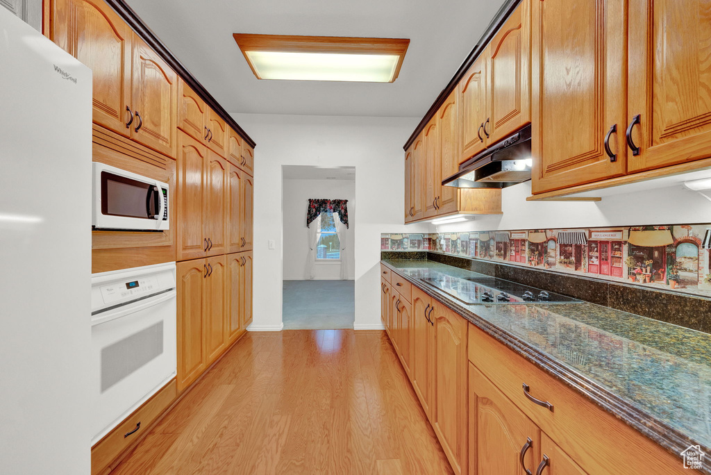 Kitchen with white appliances, dark stone countertops, and light wood-type flooring