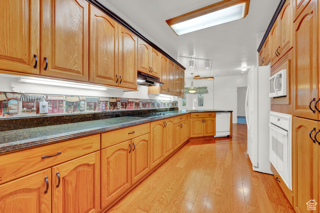 Kitchen with dark stone countertops, light hardwood / wood-style flooring, white appliances, and sink