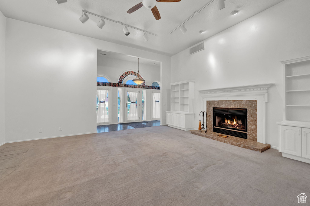 Unfurnished living room featuring rail lighting, ceiling fan, carpet floors, and a fireplace