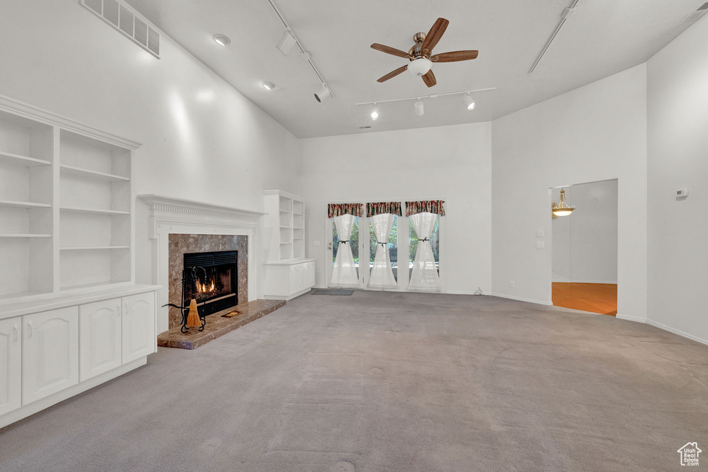 Unfurnished living room with carpet floors, ceiling fan, track lighting, and a high ceiling