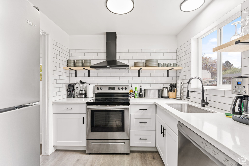 Kitchen with light hardwood / wood-style floors, wall chimney range hood, tasteful backsplash, white refrigerator, and stainless steel electric range oven