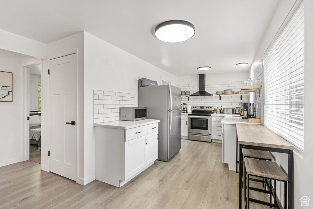 Kitchen featuring light hardwood / wood-style floors, wall chimney range hood, tasteful backsplash, and stainless steel appliances