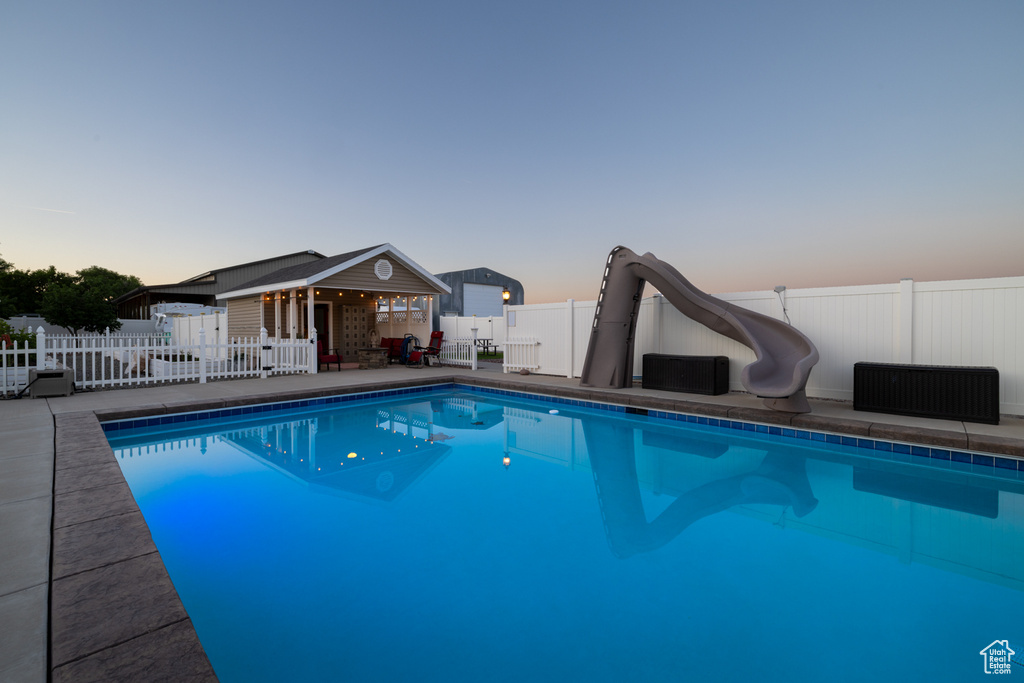 Pool at dusk featuring a fenced backyard, a water slide, and a patio