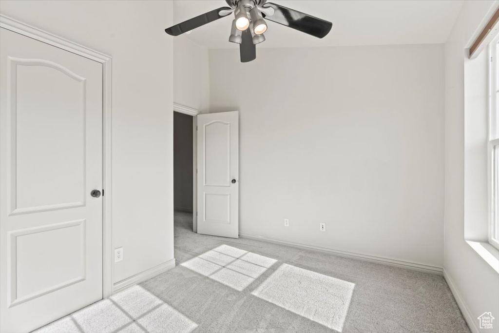 Unfurnished bedroom with ceiling fan, vaulted ceiling, and light carpet