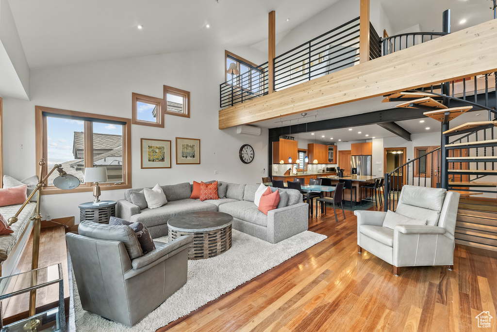 Living room featuring high vaulted ceiling, light hardwood / wood-style floors, and a wall mounted air conditioner