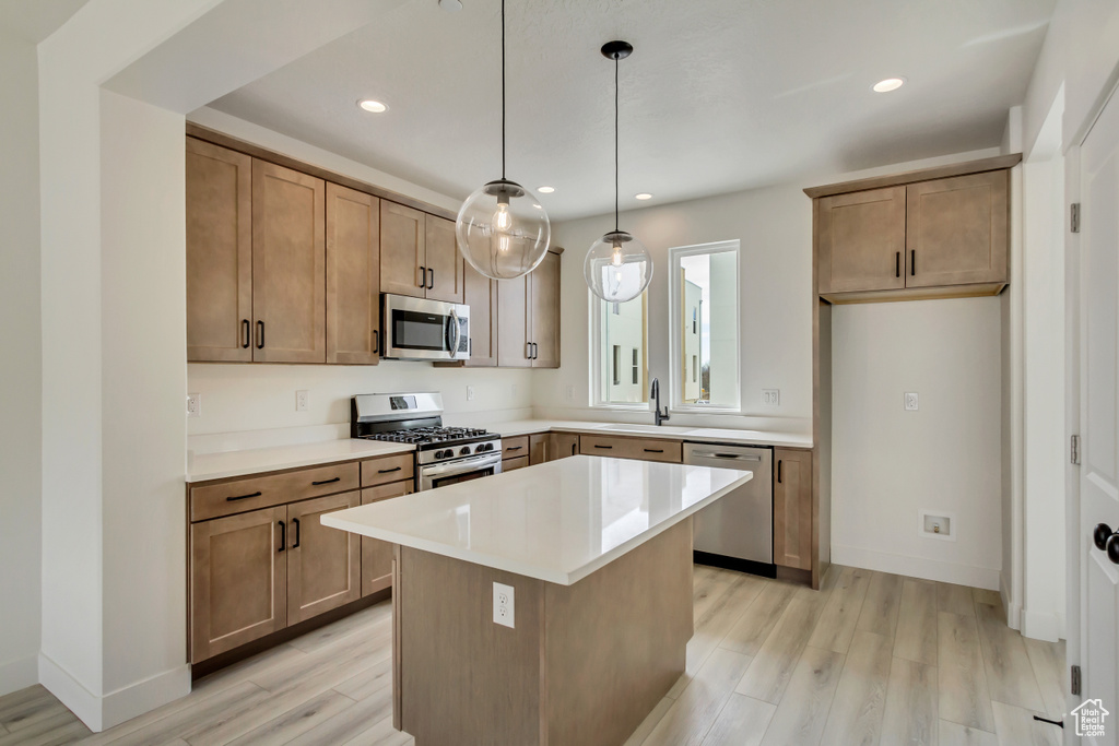 Kitchen with a center island, light hardwood / wood-style flooring, appliances with stainless steel finishes, pendant lighting, and sink