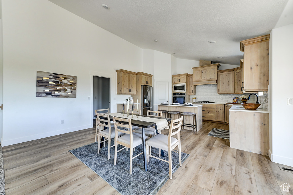 Dining room with light wood-type flooring, high vaulted ceiling, sink, and a textured ceiling