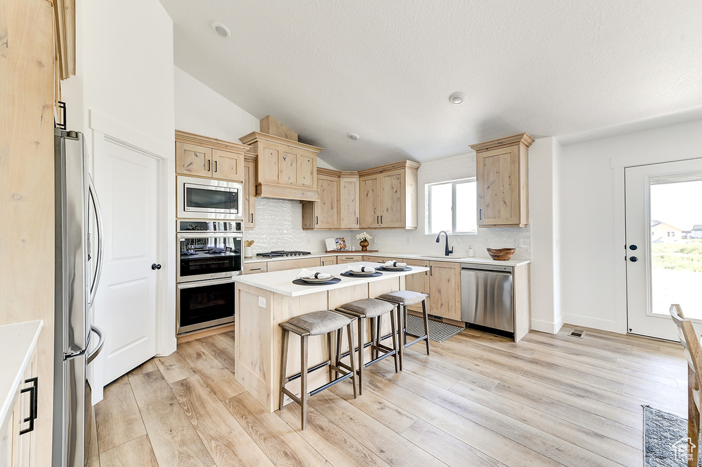 Kitchen with a kitchen island, light hardwood / wood-style flooring, appliances with stainless steel finishes, a kitchen bar, and light brown cabinets