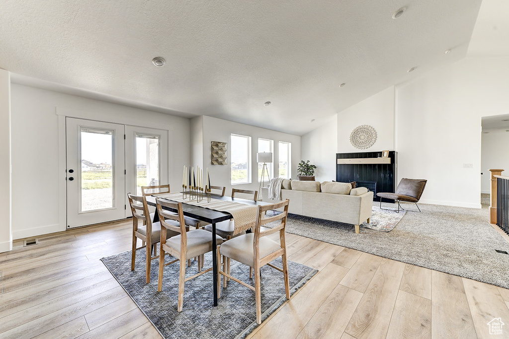 Dining space featuring a textured ceiling, vaulted ceiling, light wood-type flooring, and a multi sided fireplace