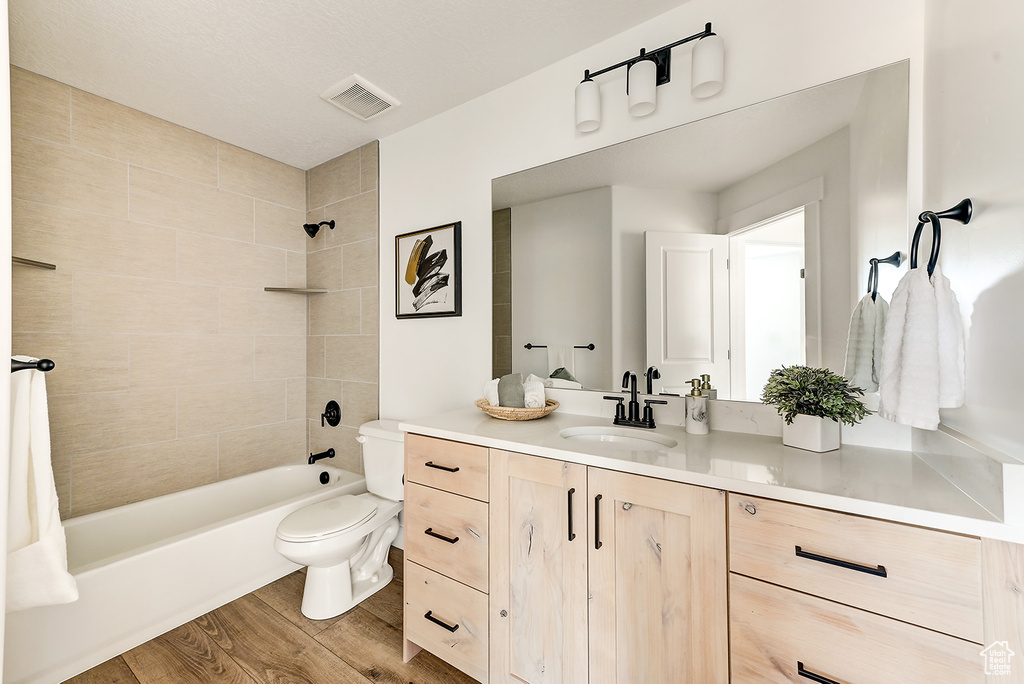 Full bathroom with toilet, hardwood / wood-style flooring, tiled shower / bath combo, and vanity