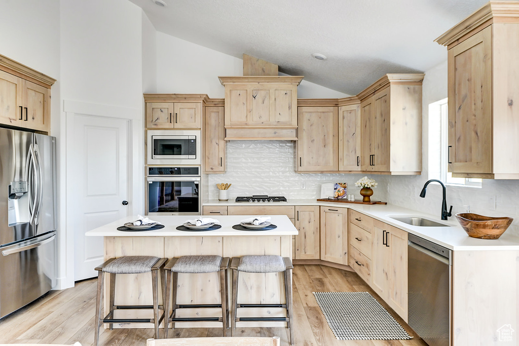 Kitchen with vaulted ceiling, light brown cabinetry, a center island, stainless steel appliances, and sink