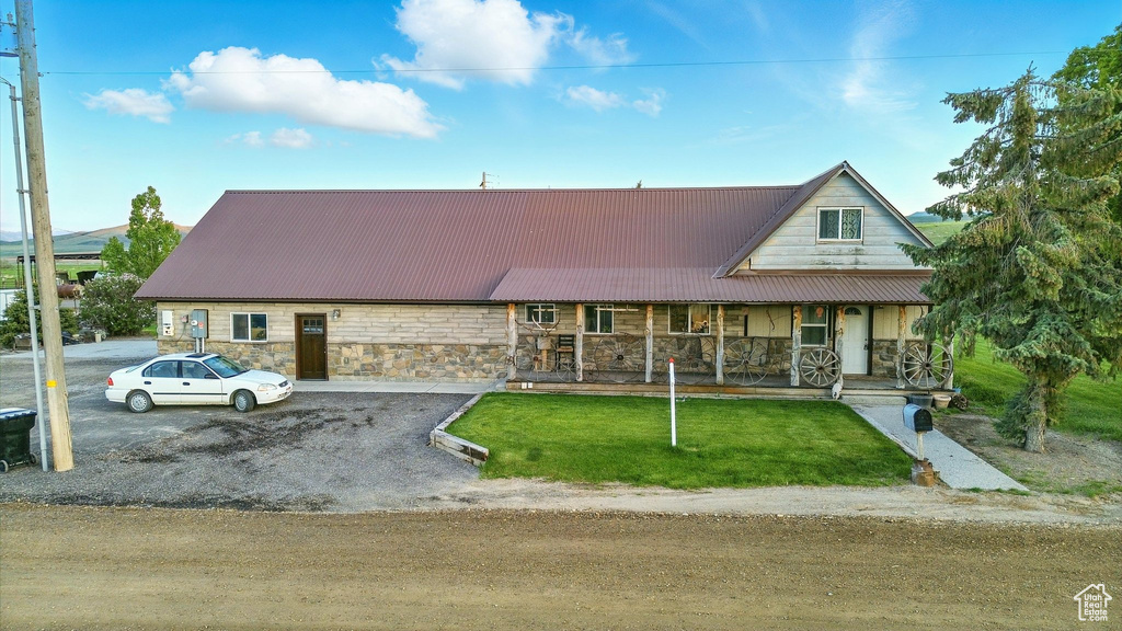 View of front of home with stone siding, a porch, a front yard, and metal roof