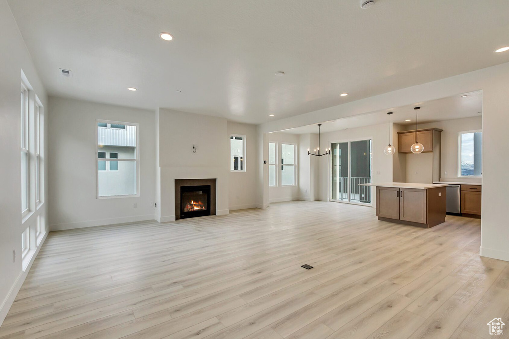 Unfurnished living room featuring light wood-type flooring and an inviting chandelier