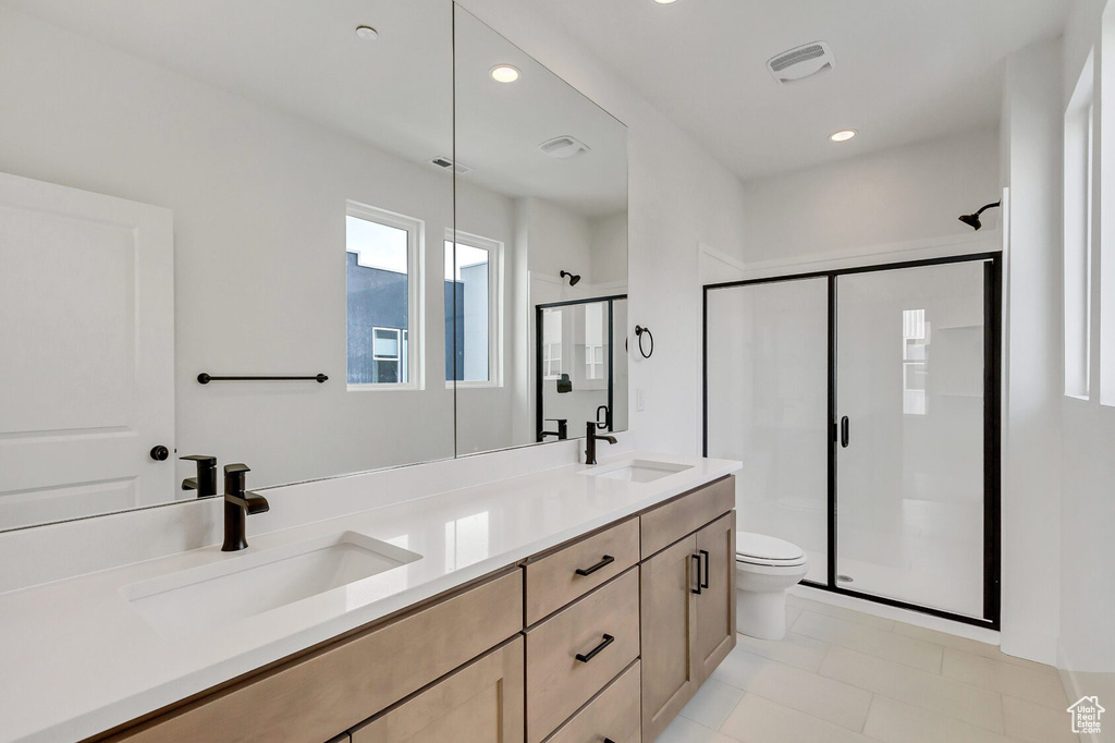 Bathroom with a shower with shower door, double vanity, tile flooring, and toilet