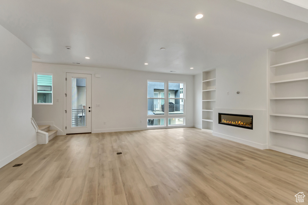 Unfurnished living room featuring light hardwood / wood-style floors, built in features, and plenty of natural light