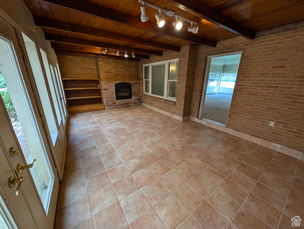 Unfurnished living room featuring wood ceiling, brick wall, a brick fireplace, track lighting, and light tile patterned flooring