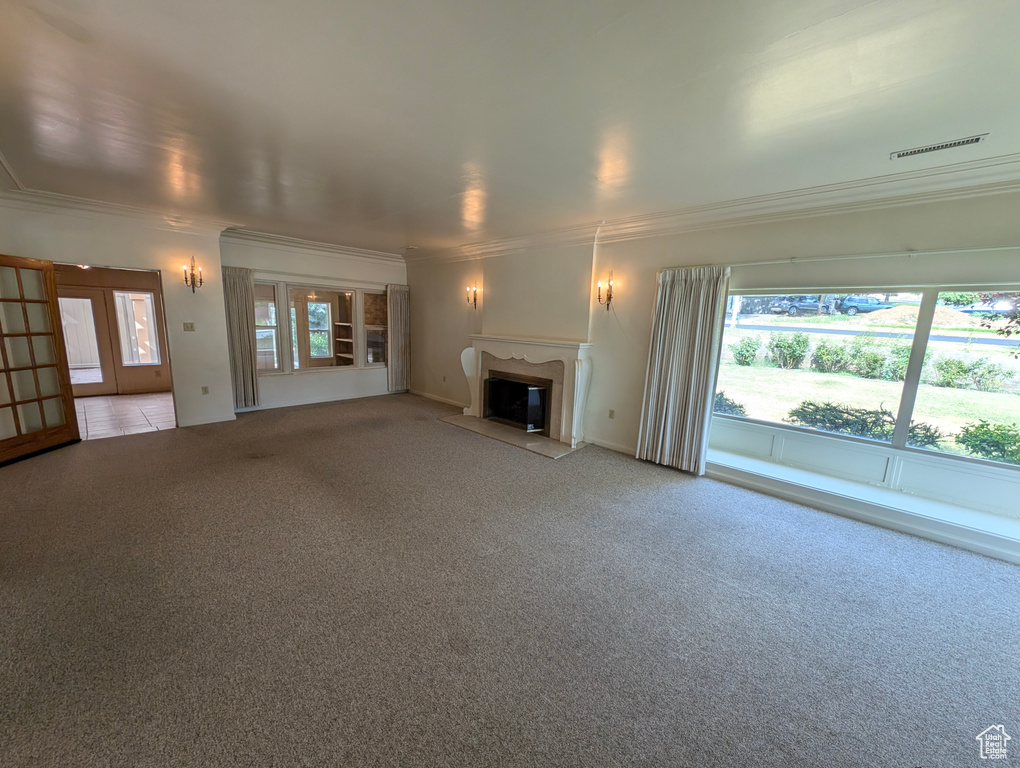 Unfurnished living room with crown molding, light colored carpet, french doors, and a premium fireplace