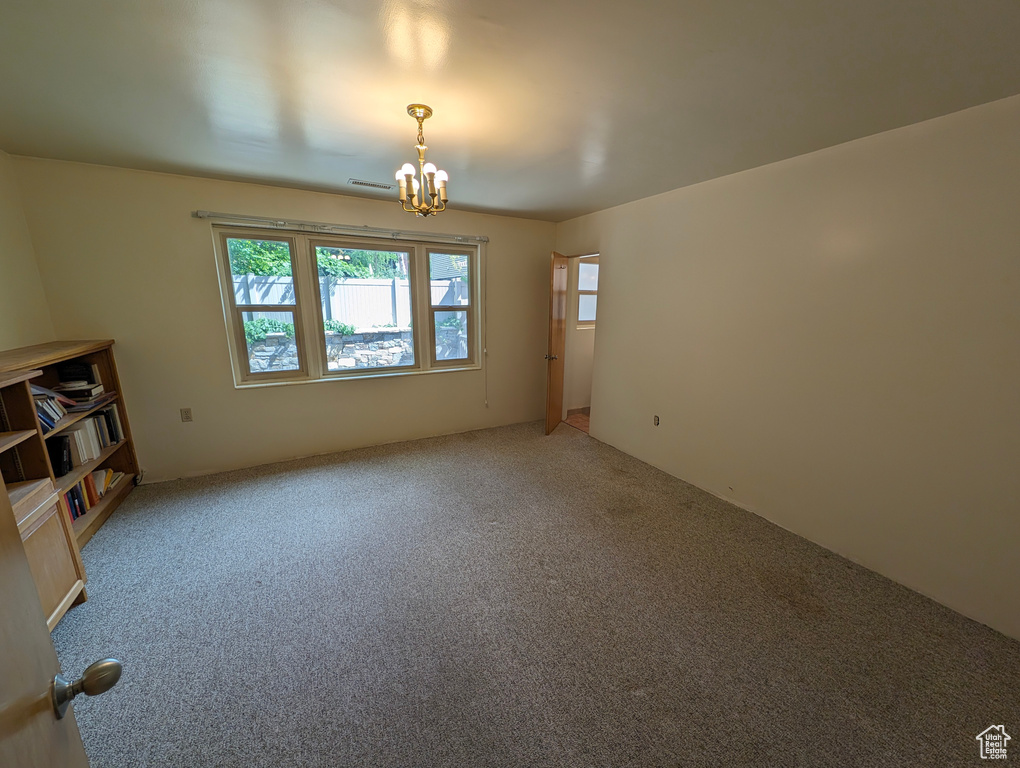 Carpeted spare room featuring an inviting chandelier and a healthy amount of sunlight