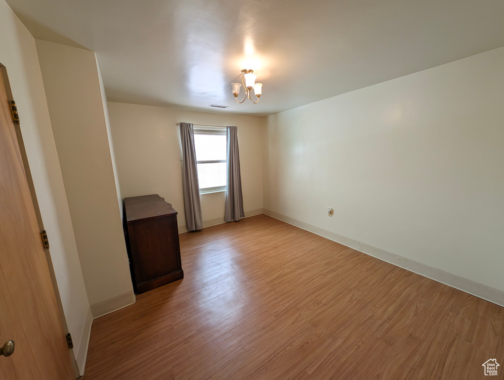 Empty room with wood-type flooring and a notable chandelier