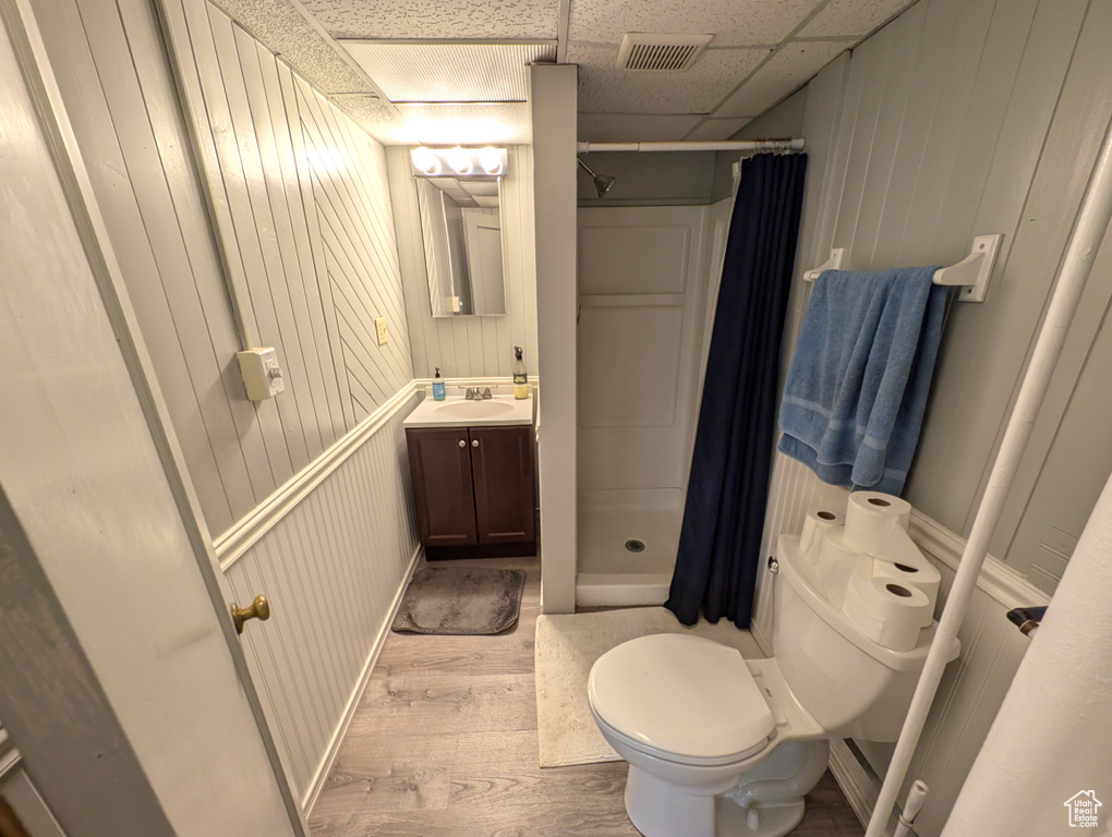 Bathroom with a drop ceiling, wood-type flooring, vanity, toilet, and walk in shower