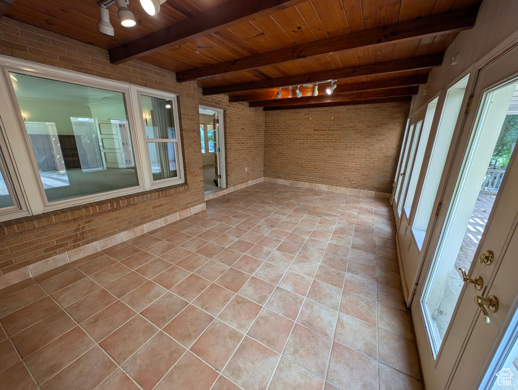 Tiled spare room featuring beam ceiling, rail lighting, wood ceiling, and brick wall