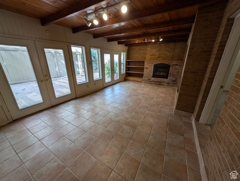 Unfurnished living room featuring brick wall, track lighting, wooden ceiling, beamed ceiling, and light tile patterned flooring