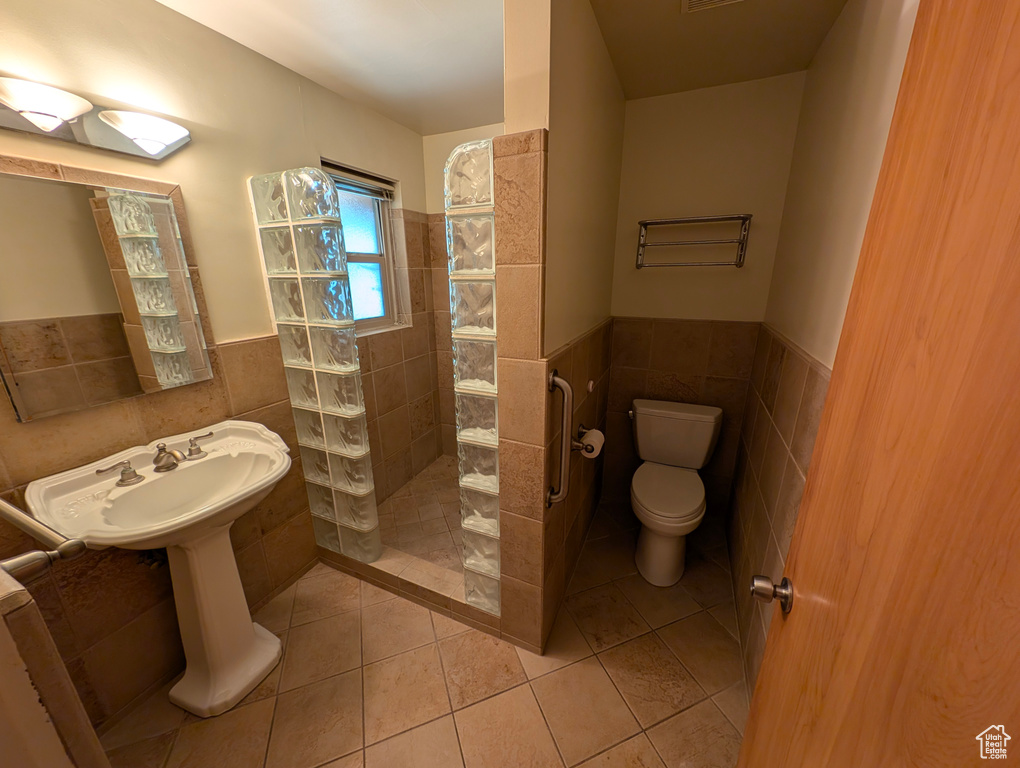 Bathroom with tile walls, toilet, a tile shower, and tile patterned floors