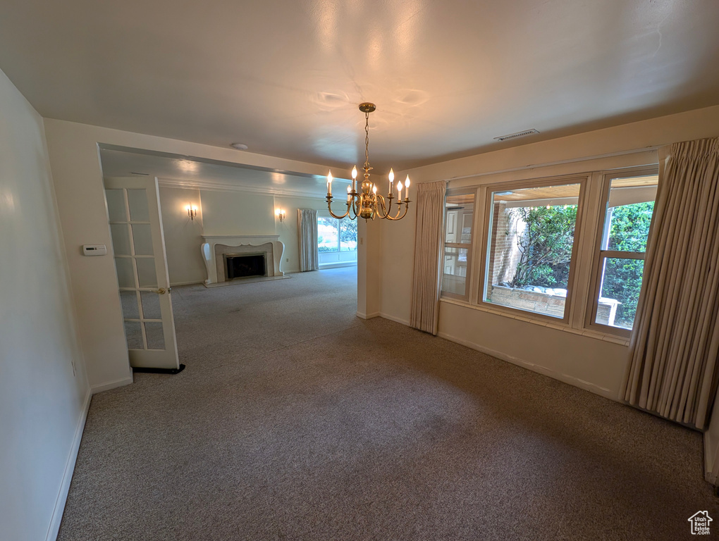 Unfurnished dining area featuring carpet flooring, an inviting chandelier, and a healthy amount of sunlight