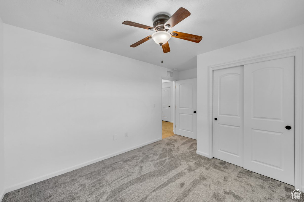 Unfurnished bedroom with ceiling fan, a closet, and light colored carpet