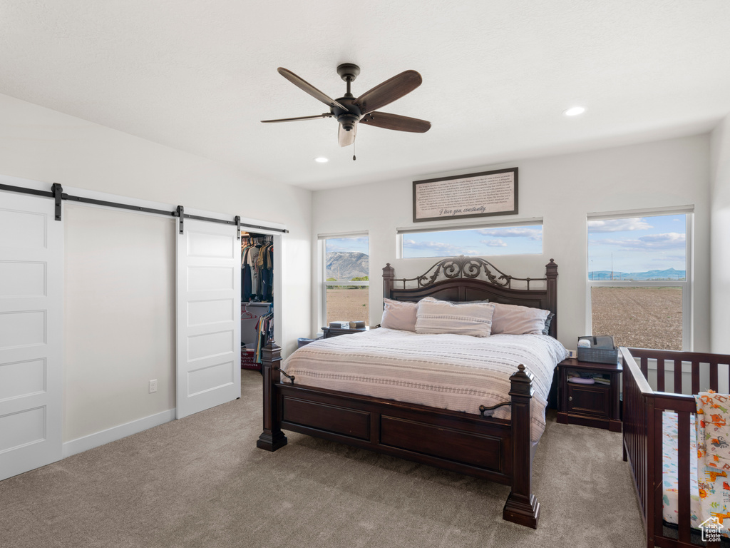 Bedroom featuring a closet, a spacious closet, a barn door, carpet flooring, and ceiling fan