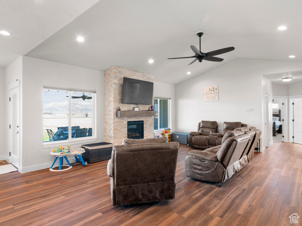 Living room with a stone fireplace, dark hardwood / wood-style flooring, ceiling fan, and vaulted ceiling